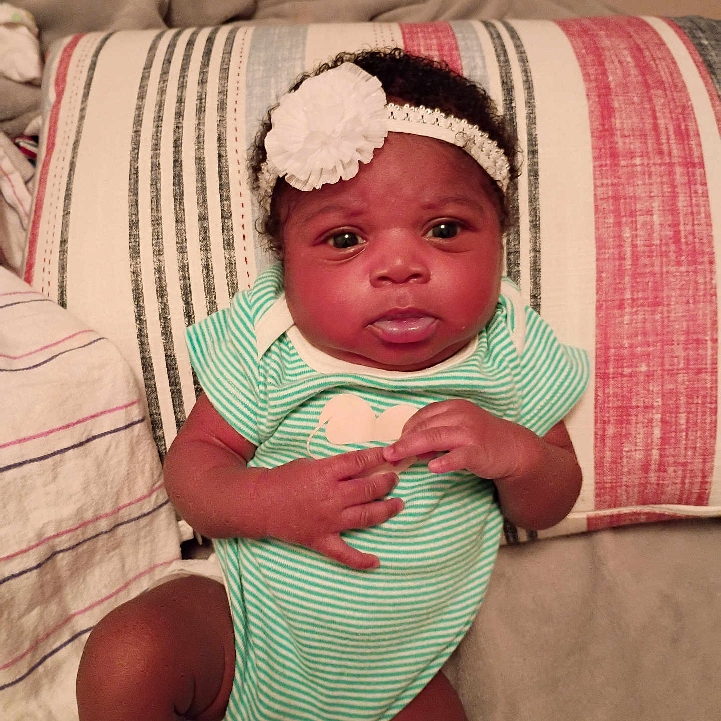 Aviana joined the competition — help win amazing prizes! baby, bed, blanket, cute, expression, face, flower, hands, headband, indoor, infant, legs, onesie, person, pillow, portrait, skin, socks, striped_clothing, striped_pillow