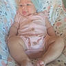 baby, infant, child, pink_outfit, headwrap, tongue_out, cushion, patterned_background, soft_lighting, cute, chubby_legs, relaxed, indoors, portrait, smiling, happy, person, closeup, baby_girl, seated