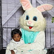 Larry is registered to the contest to win money with this photo: child, easter_bunny, costume, holiday_photo, barn_door_background, white_clothing, sitting, portrait, indoor, cute, person, face, smile, holiday, seasonal, festive, photography, baby, happy, event