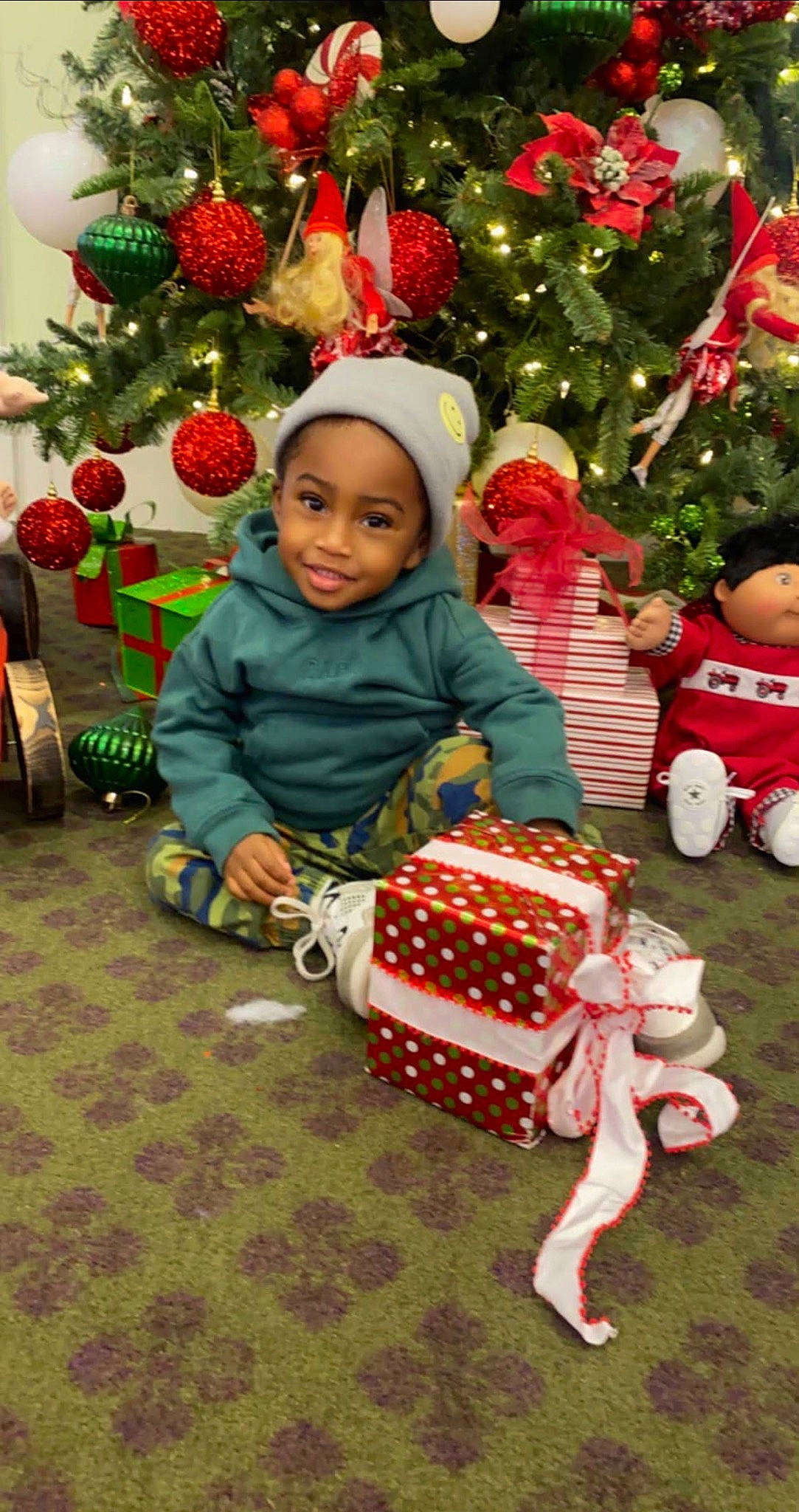 Luka is registered to the contest to win money with this photo: baby_toddler_clothing, child, christmas, christmas_decoration, christmas_eve, christmas_ornament, christmas_tree, event, green, happy, holiday, holiday_ornament, joy, lap, ornament, person, red, smile, tire, toddler