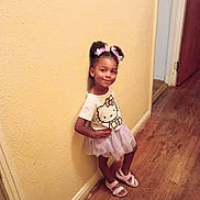 Saraiy'H is registered to the contest to win money with this photo: child, girl, smile, hello_kitty, tshirt, skirt, hair_bows, sandals, wood_floor, hallway, yellow_wall, pose, cute, indoor, person, fashion, childhood, happy, standing, playful