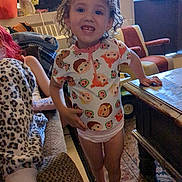 Eliza is registered to the contest to win money with this photo: child, indoor, smile, curly_hair, colorful_clothing, table, person, furniture, window, carpet, blanket, seated_person, leopard_print, living_room, toy, casual_pose, barefoot, happy, young_child