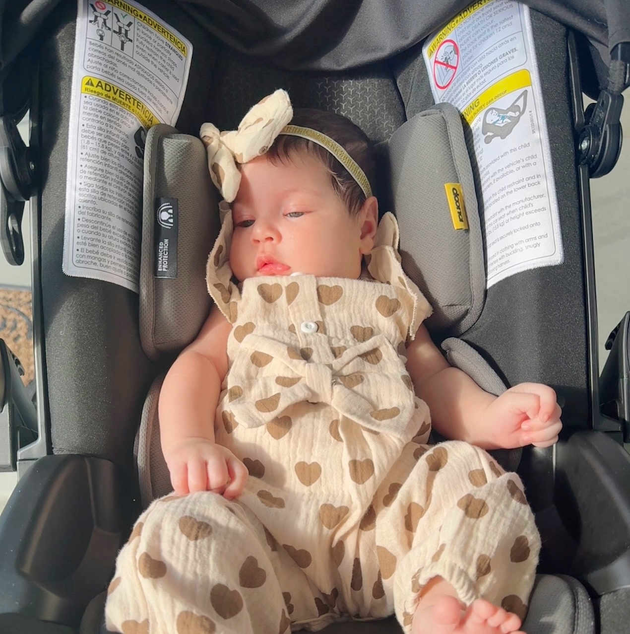Charlotte is registered to the contest to win money with this photo: baby, infant, car_seat, heart_pattern, romper, headband, sleepy, child, soft_light, indoors, seat_belt, safety, cute, adorable, clothing, newborn, person, resting, toddler, close_up