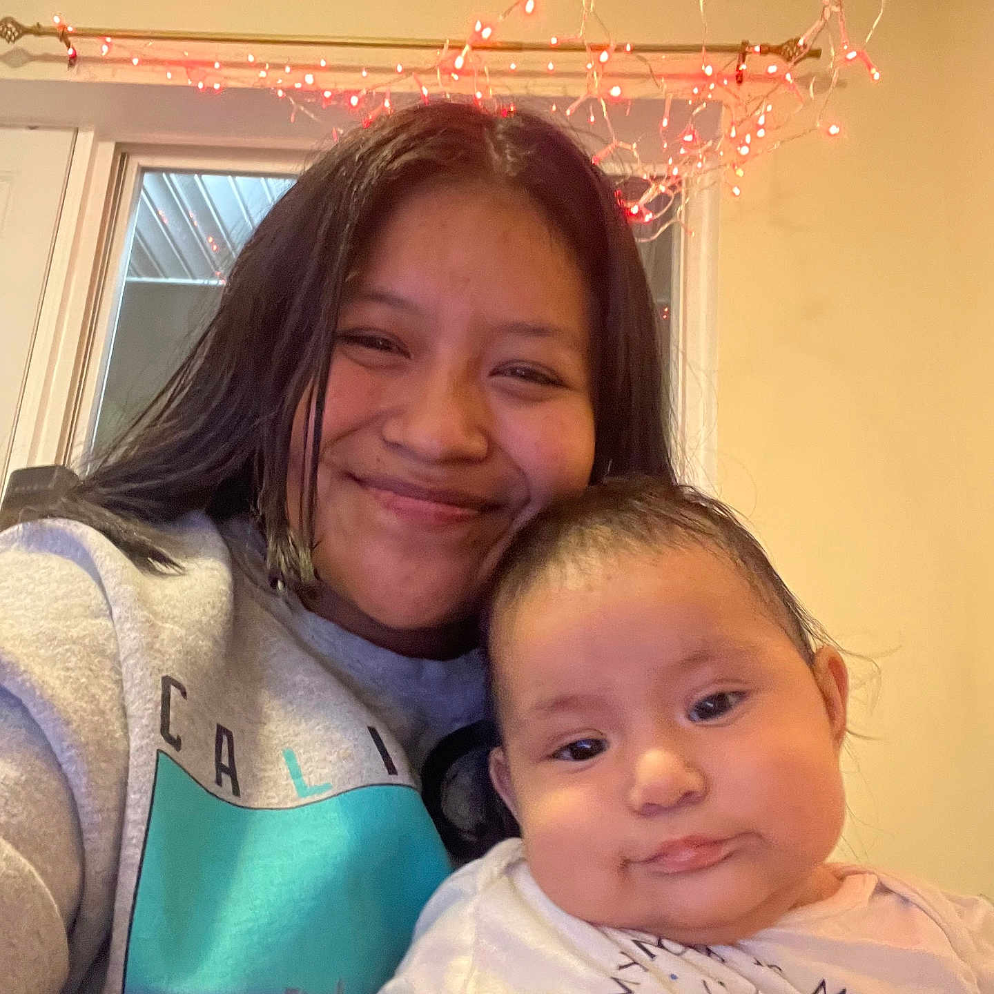 Tania joined the competition — help win amazing prizes! baby, casual_clothing, child, cozy, cute, family, happy, holding, home, indoor, infant, lights, long_hair, person, portrait, red_lights, smile, sweatshirt, window, woman