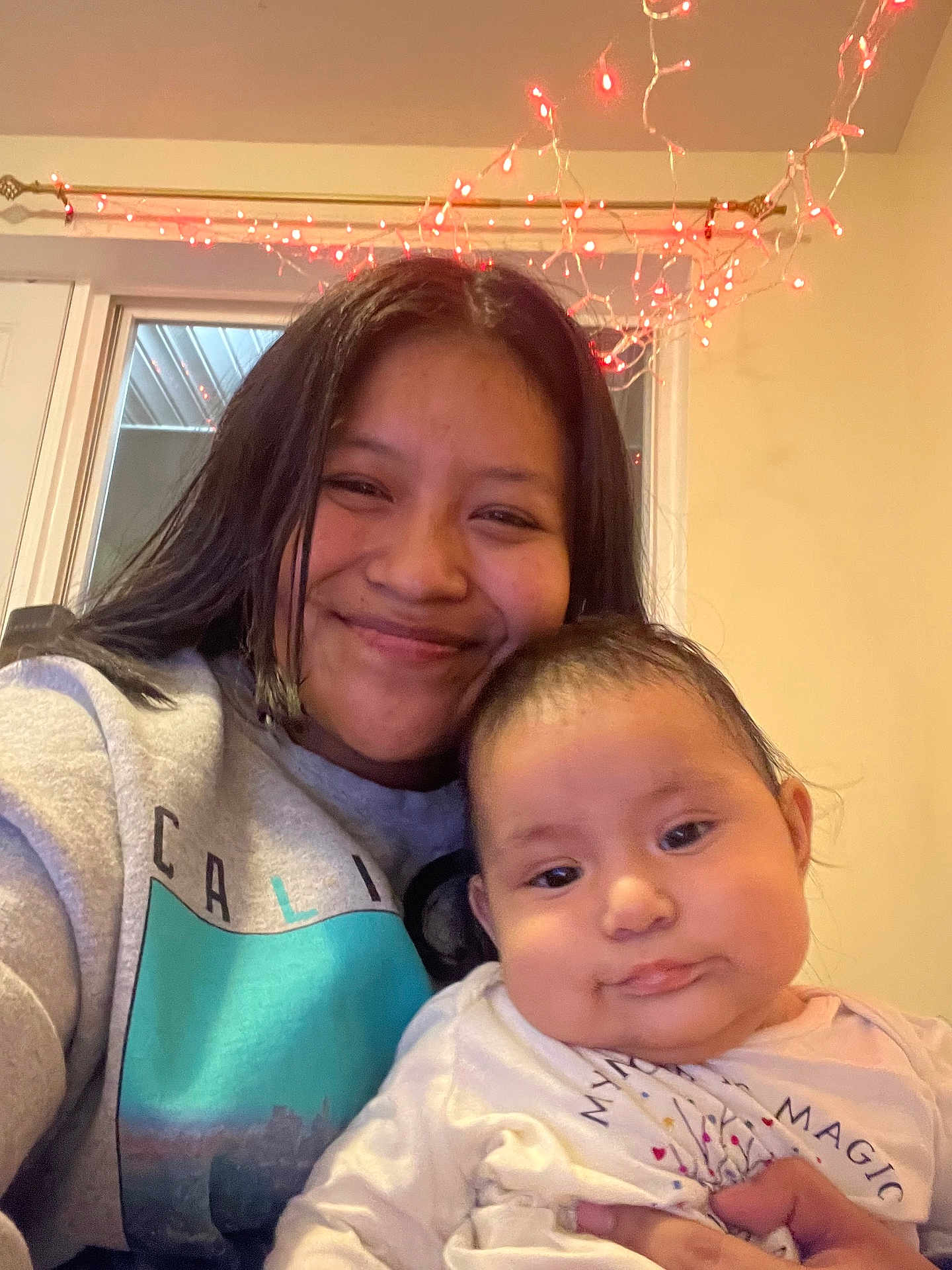 Tania joined the competition — help win amazing prizes! woman, baby, smile, indoor, portrait, family, person, child, long_hair, sweatshirt, window, lights, red_lights, holding, cozy, casual_clothing, happy, cute, infant, home