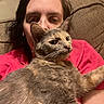 Reese is registered to the contest to win money with this photo: animal, casual, cat, close_up, comfort, companion, couch, face, fur, home, human, indoor, person, pet, red_shirt, relaxed, resting, seated, tortoiseshell_cat, whiskers