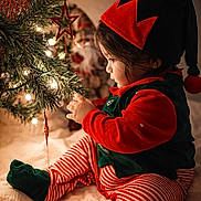 Vaayu is registered to the contest to win money with this photo: toddler, child, christmas_tree, christmas_lights, christmas_ornaments, elf_costume, holiday, festive, decorations, indoor, seasonal, toy, red_and_green, striped_pants, hat, cute, portrait, warm_lighting, celebration, santa_figurine