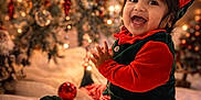 Vaayu is registered to the contest to win money with this photo: baby, child, smiling, holiday, christmas_tree, christmas_ornaments, elf_costume, red_and_green, striped_pants, festive, indoors, happy, clapping, blanket, decorations, cute, portrait, celebration, seasonal, warm_lighting