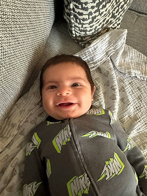 Luis is registered to the contest to win money with this photo: baby, child, comfort, face, facial_expression, fashion_accessory, fun, happy, hat, joy, linens, pattern, person, personal_protective_equipment, sitting, sleeve, smile, sun_hat, t_shirt, toddler