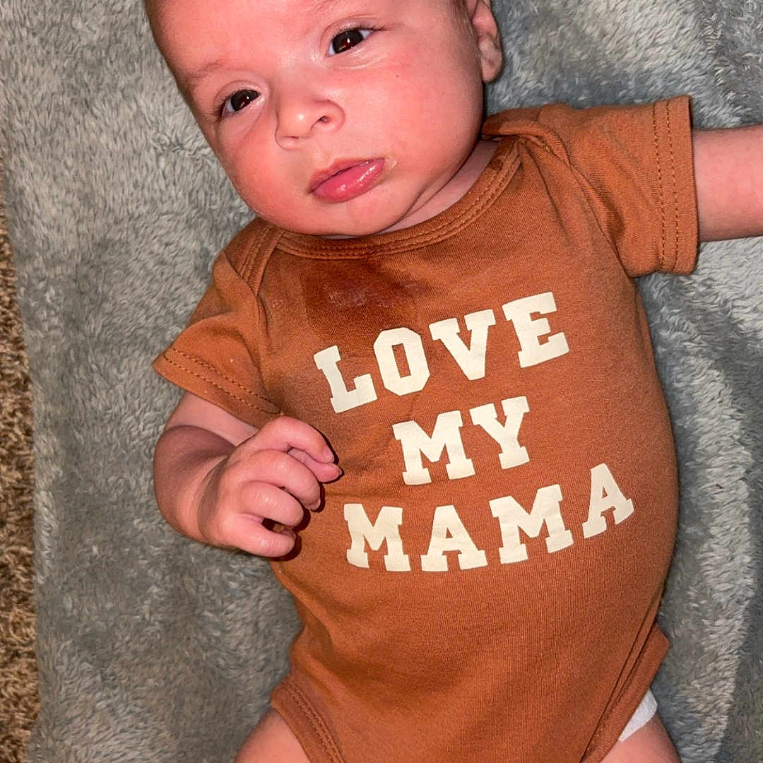 Malakai joined the competition — help win amazing prizes! baby, infant, onesie, clothing, blanket, soft_texture, lying_down, cute, expression, face, skin, hand, foot, newborn, child, person, indoor, portrait, love, mama