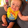 baby, child, smiling, yellow_shirt, tank_top, sitting, couch, indoor, happy, cute, infant, casual_clothing, shorts, barefoot, portrait, light, home, relaxed, funny_expression, person