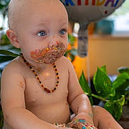 James joined the competition — help win amazing prizes! baby, birthday, cake, messy, frosting, blue_eyes, diaper, necklace, balloon, celebration, indoor, plants, child, happy, cute, portrait, sitting, food, colorful, smudged