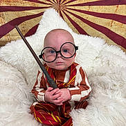 Axel joined the competition — help win amazing prizes! baby, child, glasses, wand, striped_clothing, red_tie, white_blanket, fluffy, portrait, indoor, magical, costume, cute, serious_expression, sitting, toy, background_pattern, round_glasses, infant, closeup