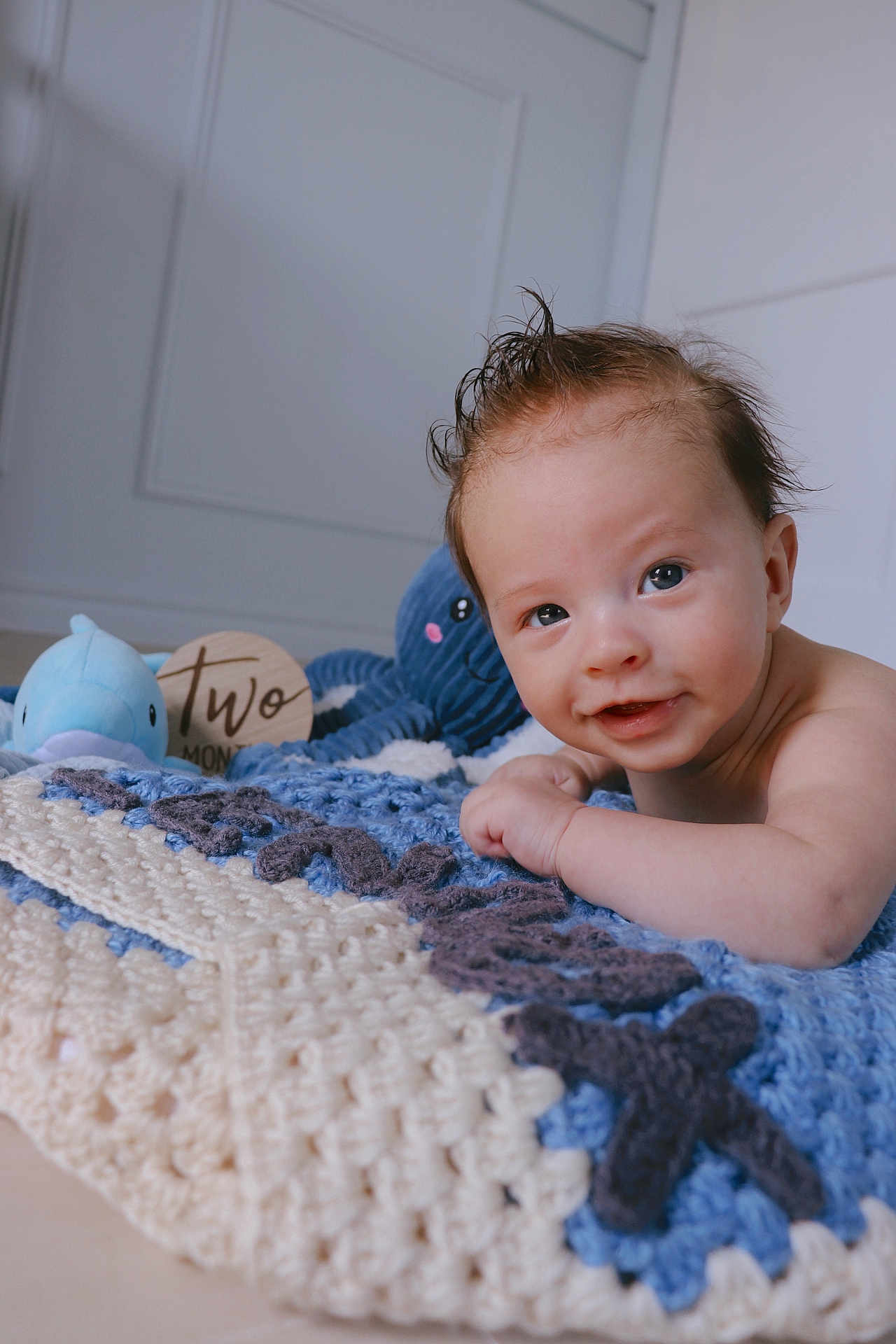Lennox is registered to the contest to win money with this photo: baby, infant, smile, face, blue_eyes, crocheted_blanket, plush_toys, octopus_toy, dolphin_toy, wooden_sign, two_months, indoor, floor, cute, child, portrait, happy, skin, hair, playful