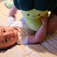 Richie joined the competition — help win amazing prizes! baby, plush_toy, bed, child, soft_lighting, toy, cute, smile, face, indoors, blanket, white_clothing, person, infant, resting, playful, home, comfort, childhood, cozy