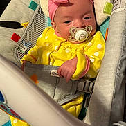 Remi is registered to the contest to win money with this photo: baby, infant, child, portrait, pacifier, pink_bow, yellow_outfit, polka_dots, bouncer, baby_seat, sitting, awake, face, hands, indoor, colorful, textile, harness, nursery, closeup