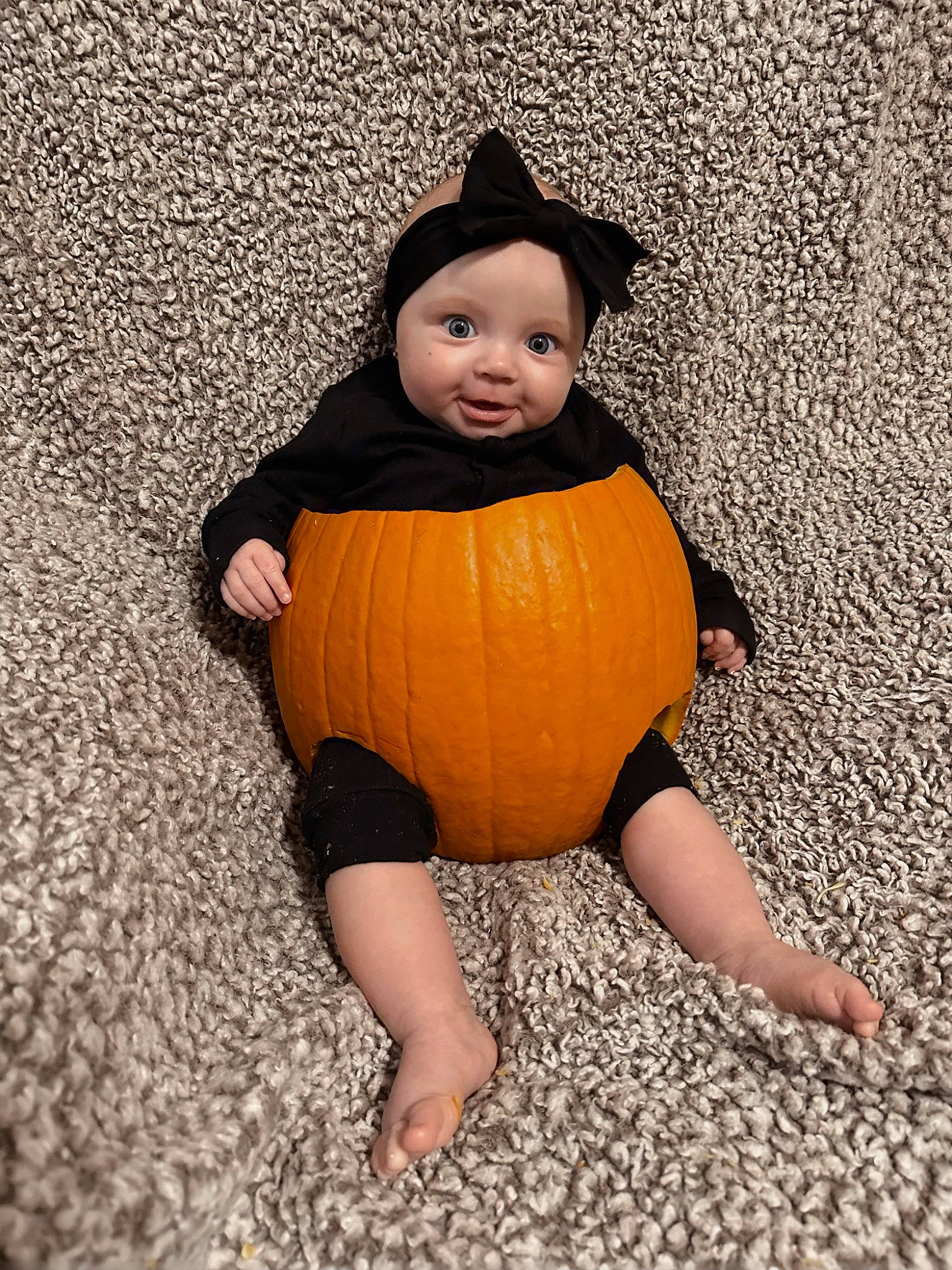 Kinley is registered to the contest to win money with this photo: arm, baby, baby_toddler_clothing, calabaza, eye, face, flooring, foot, happy, hat, head, headwear, human_body, human_leg, orange, person, pumpkin, sleeve, thigh, toddler