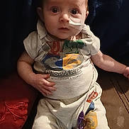 Alexa is registered to the contest to win money with this photo: baby, child, infant, face, medical_tube, nasal_tube, hospital, couch, clothing, sitting, indoors, person, cute, young, expression, soft_lighting, blanket, pajamas, comfort, home