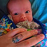 Serenity joined the competition — help win amazing prizes! baby, infant, child, portrait, wide_eyes, blanket, colorful, swaddled, hand, adult_hand, tattoo, close_up, face, indoors, cozy, fabric, blue_background, seated, family, photography