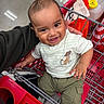 baby, cartoon, child, clothing, eyes, face, grocery_store, happy, indoor, infant, metal, pants, parent, portrait, red, shirt, shopping_cart, sitting, smiling, supermarket