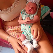 Nalia participe au concours pour gagner de l'argent avec cette photo : baby, newborn, infant, sleeping, headband, flower, onesie, socks, person, adult, holding, hands, couch, red_couch, indoor, footwear, slippers, skin, closeup, seated