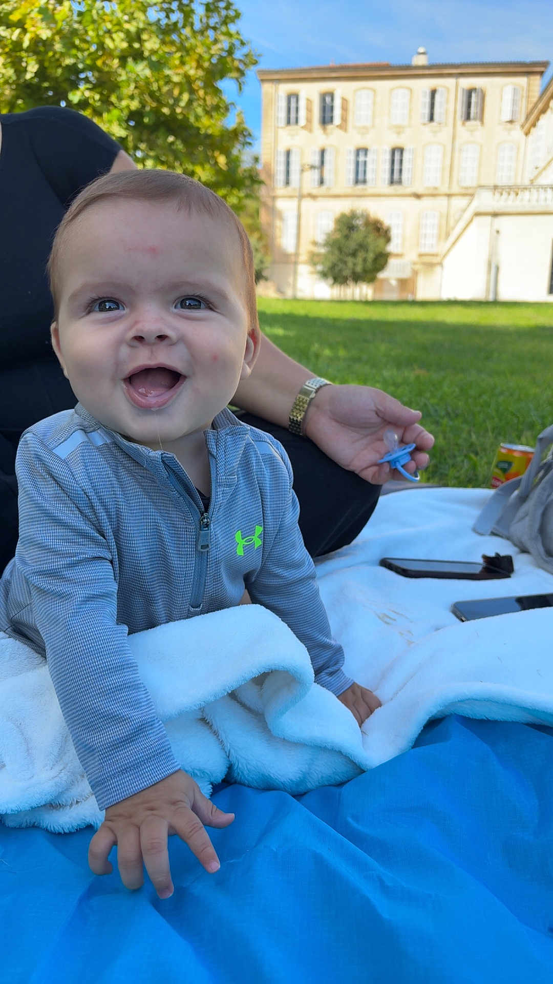 Ilyass participe au concours pour gagner de l'argent avec cette photo : baby, child, smiling, outdoor, grass, blanket, pacifier, person, hand, clothing, building, daylight, happy, face, crawling, jacket, nature, park, blue_sky, relaxation