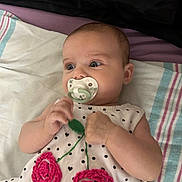 Arya is registered to the contest to win money with this photo: baby, bedding, blanket, child, crocheted_flowers, cute, dress, face, green_toy, hands, head, indoor, infant, lying_down, pacifier, polka_dots, portrait, striped_blanket, toy, wide_eyes