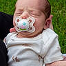 baby, newborn, sleeping, pacifier, outdoor, grass, portrait, close_up, infant, white_clothing, onesie, cradled, peaceful, face, head, hand, arm, parent, nature, photography