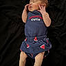 newborn, baby, infant, sleeping, portrait, lying_down, black_background, blue_outfit, baby_clothes, skirt, strawberry_pattern, hands, face, closed_eyes, peaceful, cute, indoor, photography, text_on_clothing, child