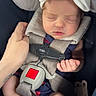 newborn, baby, sleeping, infant, car_seat, safety_harness, bow, headband, pacifier, caregiver, hand, portrait, close_up, indoors, vehicle, blanket, clothing, socks, peaceful, family