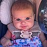 baby, baby_clothing, blanket, blue, bows, car_seat, child, close_up, cozy, eyes, face, head, indoor, infant, looking_at_camera, pacifier, pink, portrait, seated, smiling