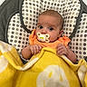 baby, infant, child, portrait, sitting, bouncer, pacifier, blanket, yellow_blanket, orange_clothing, polka_dot, wide_eyed, indoors, close_up, face, hands, smiling_blanket, baby_furniture, cozy, photography