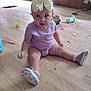 baby, child, indoor, floor, toy, sippy_cup, bow, pink_shoes, purple_clothing, wooden_floor, playtime, cute, sitting, curious, headband, infant, person, room, scattered_toys, footwear