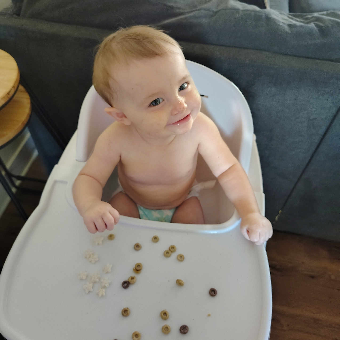 Isabella is registered to the contest to win money with this photo: baby, cereal, child, cute, diaper, face, furniture, happy, high_chair, home, indoor, living_room, messy, person, playful, seat, smile, table, wood_floor, young_child