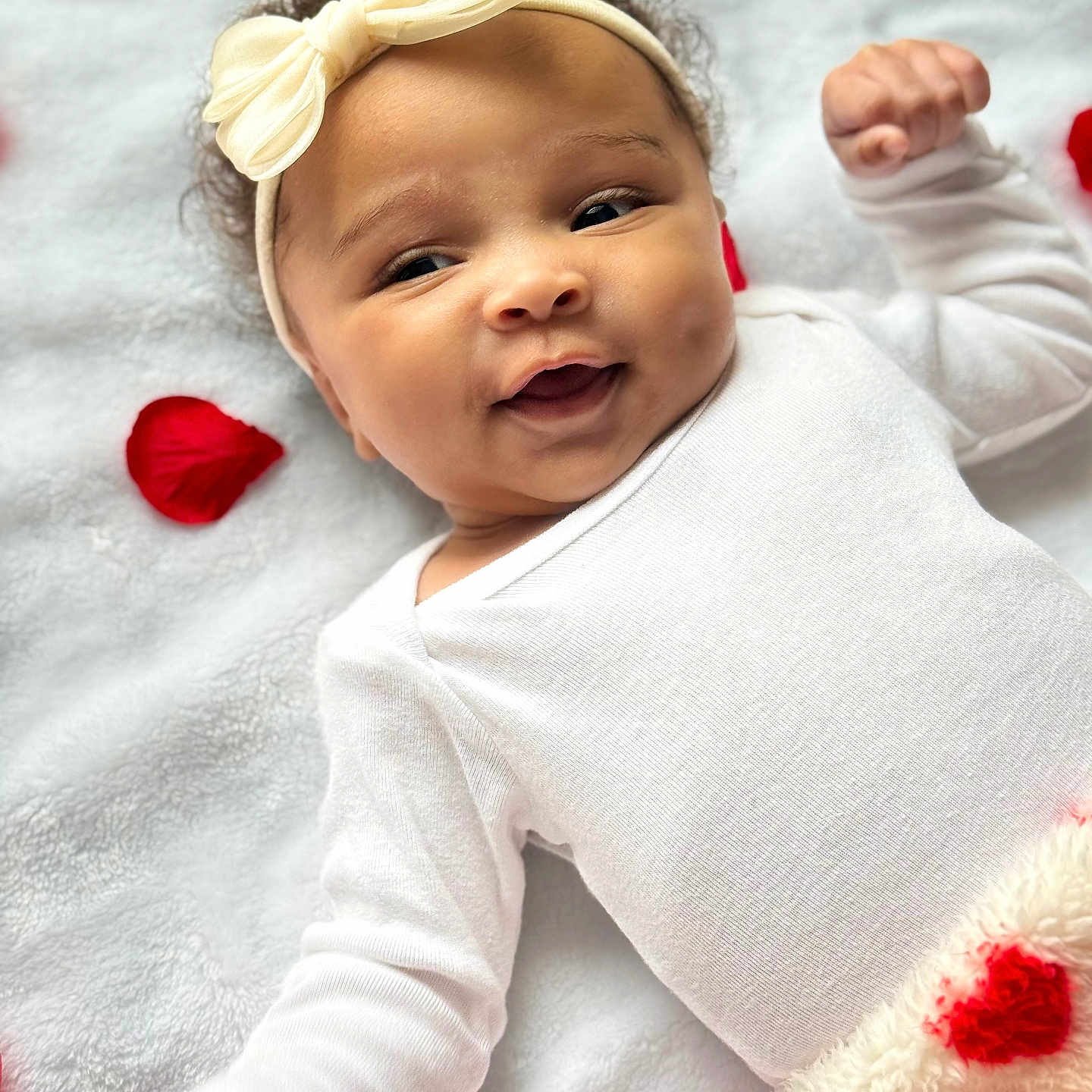 Daylee is registered to the contest to win money with this photo: adorable, baby, blanket, bow, child, closeup, cozy, cute, happy, headband, indoor, infant, lying_down, newborn, portrait, red_rose_petals, smile, soft_texture, warm, white_clothing