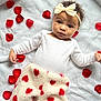 baby, infant, headband, bow, red_rose_petals, white_blanket, fleece_blanket, red_hearts, laying_down, curious_expression, soft_texture, cute, cozy, portrait, child, indoors, person, closeup, adorable, warm