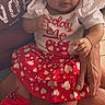 Aurora is registered to the contest to win money with this photo: baby, child, infant, red_bow, heart_pattern, red_skirt, red_shoes, white_shirt, person, sitting, indoor, clothing, cute, small_hands, legs, face, headwear, lap, adult_hand, curious