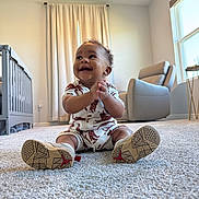 Kai joined the competition — help win amazing prizes! infant, baby, smiling, sitting, clapping_hands, onesie, patterned_clothing, sneakers, shoe_soles, carpet, nursery, crib, armchair, curtains, window, soft_light, indoor, happy, portrait, playful