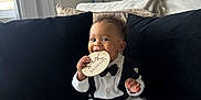 Kai is registered to the contest to win money with this photo: baby, infant, smiling, milestone_disk, bow_tie, white_outfit, sitting, sofa, couch, pillow, black_pillow, living_room, window, curtain, indoor, portrait, teething, wooden_prop, cozy, cute