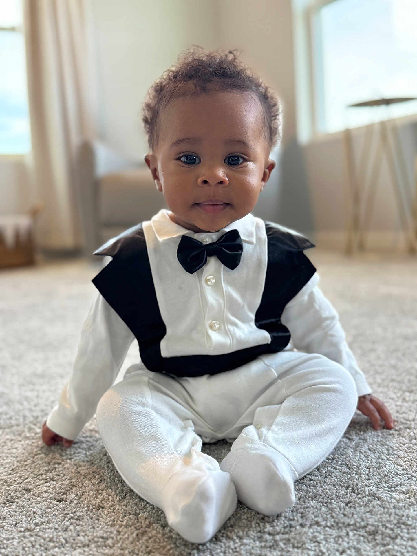 Kai joined the competition — help win amazing prizes! baby, infant, child, onesie, bow_tie, tuxedo, sitting, carpet, portrait, indoor, curly_hair, big_eyes, cute, adorable, hands, feet, soft_lighting, bokeh_background, nursery, smile