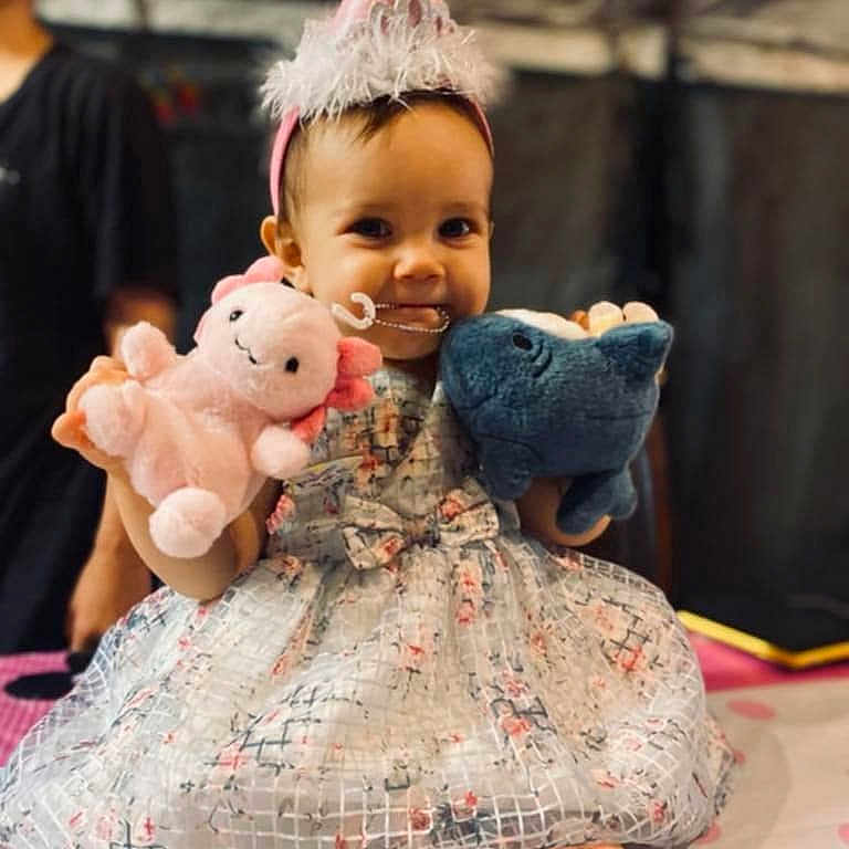 Kaipolani is registered to the contest to win money with this photo: baby, barefoot, blue, celebration, child, cute, dress, fun, happy, headband, indoor, party_hat, person, pink, plush_toy, portrait, sitting, smiling, toddler, toy