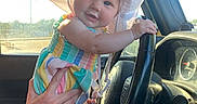 Hazel is registered to the contest to win money with this photo: baby, car_interior, child, colorful_clothing, dashboard, hand, happy, hat, keys, person, playing, portrait, seat, smiling, steering_wheel, sunlight, tattoo, vehicle, white_hat, window