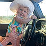 Hazel is registered to the contest to win money with this photo: baby, child, hat, white_hat, colorful_clothing, steering_wheel, car_interior, hand, tattoo, sunlight, smiling, portrait, person, vehicle, dashboard, keys, seat, window, happy, playing