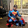 Marlo is registered to the contest to win money with this photo: animal, bench, blue_suit, companionship, costume, crouching, dog, human, indoor_lighting, man, matching_outfits, night, outdoor, pet, pet_owner, red_cape, superhero, superman_costume, window, wooden_deck