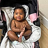 baby, infant, car_seat, blanket, diaper, curly_hair, smiling, happy, indoors, floor, wooden_floor, black_hair, cute, child, person, skin, foot, hand, seat, soft