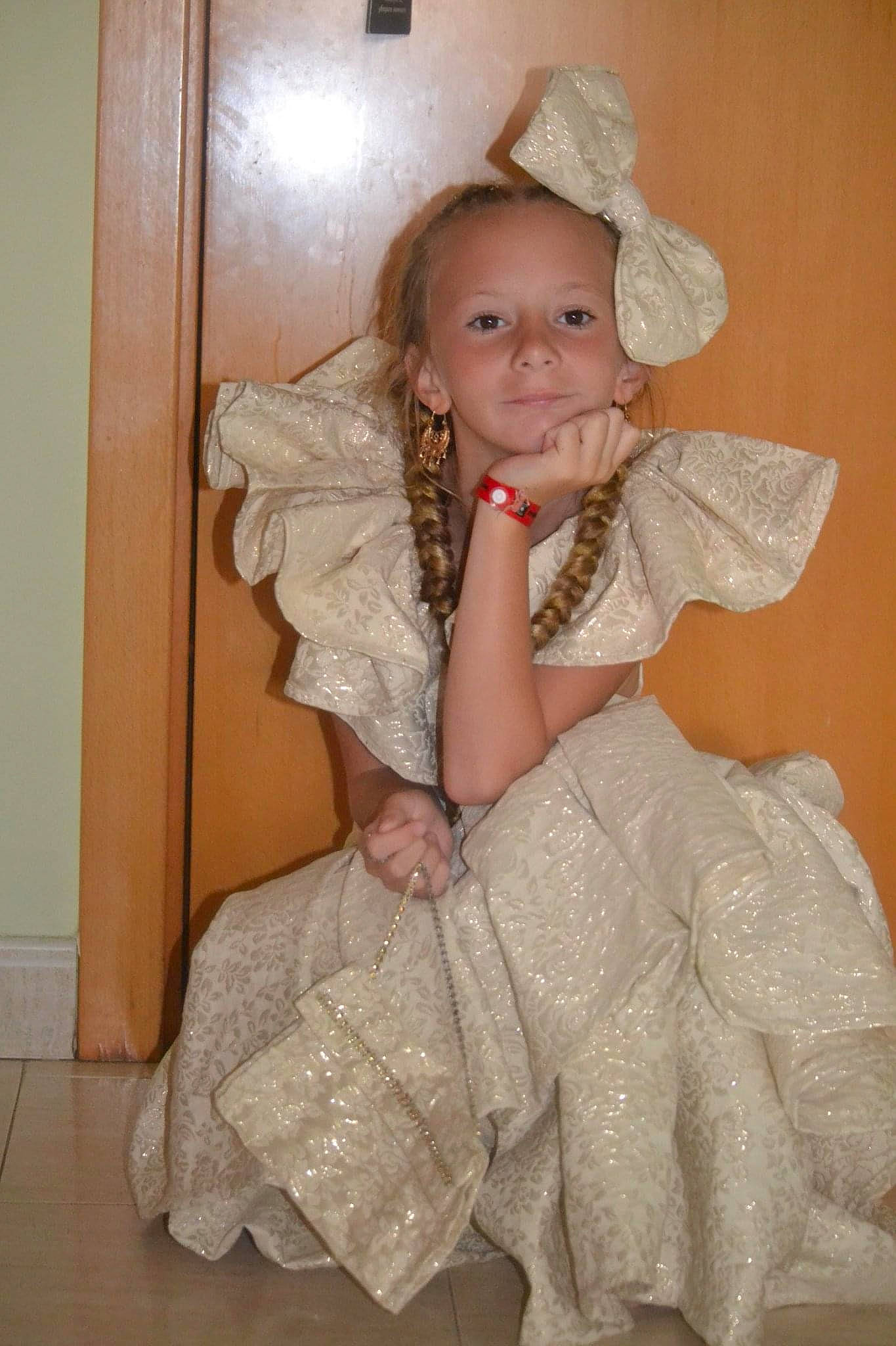 Faithy a rejoint le concours — aidez-le/la à gagner de superbes lots ! baby_toddler_clothing, bridal_accessory, child, dress, embellishment, event, fashion_design, formal_wear, fun, hairstyle, happy, hat, one_piece_garment, person, ruffle, skin, sleeve, smile, standing, textile