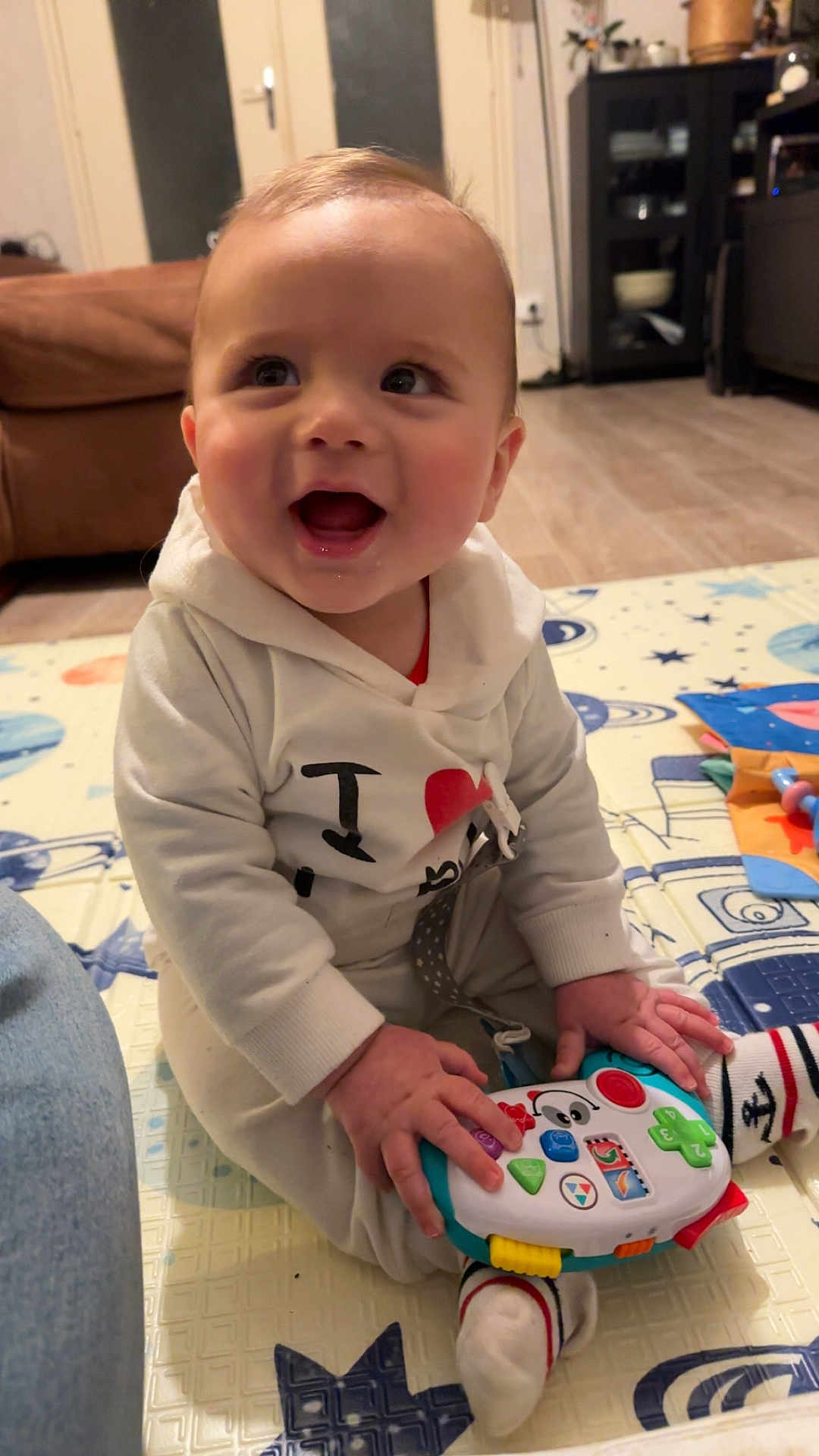 Milan a rejoint le concours — aidez-le/la à gagner de superbes lots ! baby, child, toy, play_mat, hoodie, smiling, indoor, floor, colorful, sitting, happy, person, sock, furniture, living_room, wood_floor, cabinet, door, cute, play