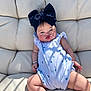 Holland is registered to the contest to win money with this photo: baby, child, headband, bow, onesie, cushion, chair, plush, skin, face, expression, sunlight, shadow, sitting, cute, infant, small_hand, legs, casual, indoor