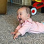 baby, child, infant, carpet, pink_clothing, toy_vehicle, red_toy, yellow_seat, crawling, happy, smiling, indoor, carpet_texture, bracelet, hair_clip, floor, playtime, furniture, home, cute