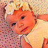 baby, infant, face, headband, flower, cute, skin, eyes, smile, lying_down, blanket, pattern, colorful, clothing, arm, hand, newborn, child, portrait, closeup